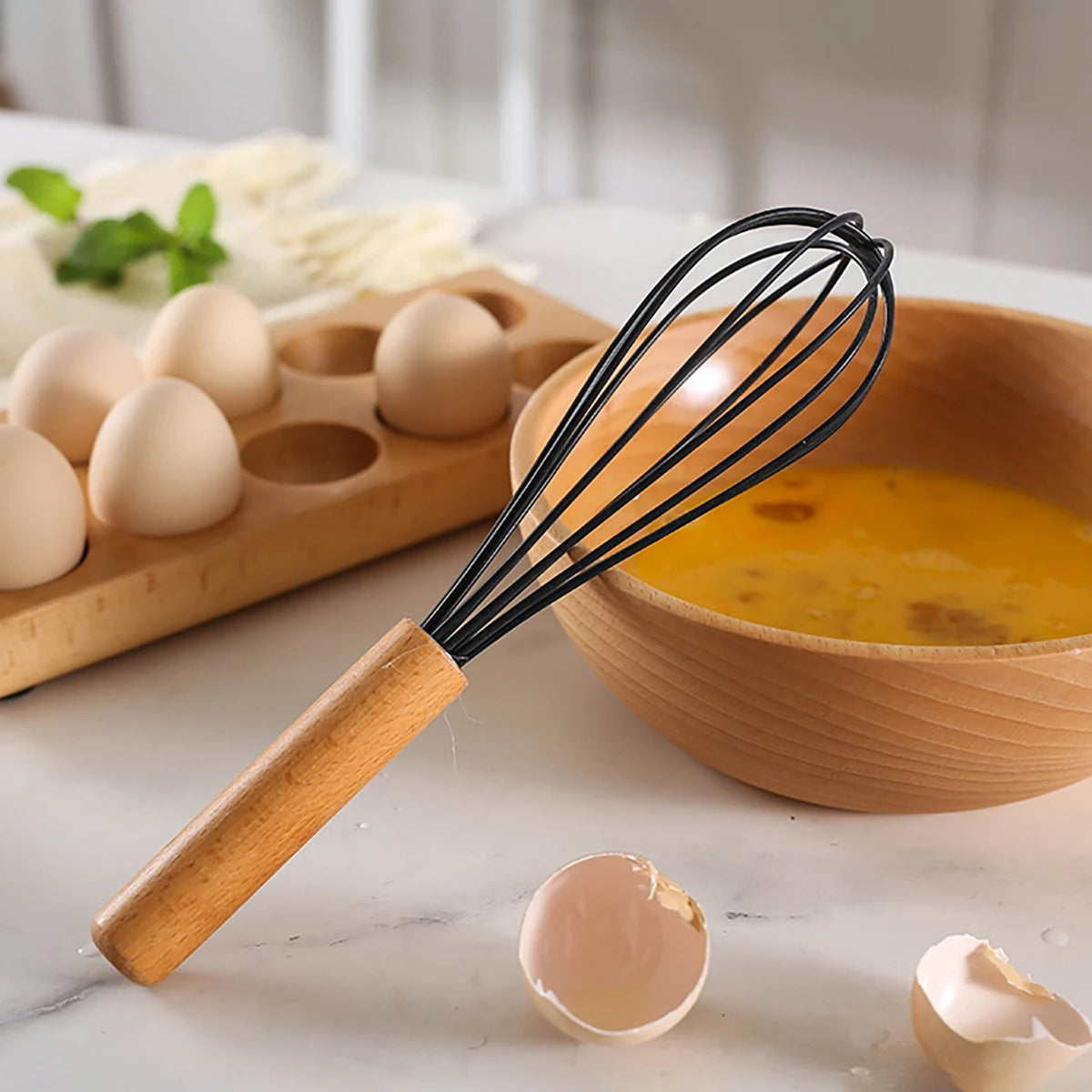 Wooden whisk with a bowl of eggs and a wooden board with eggs on a marble surface. silicone wooden handle kitchen utensil set Pakistan.