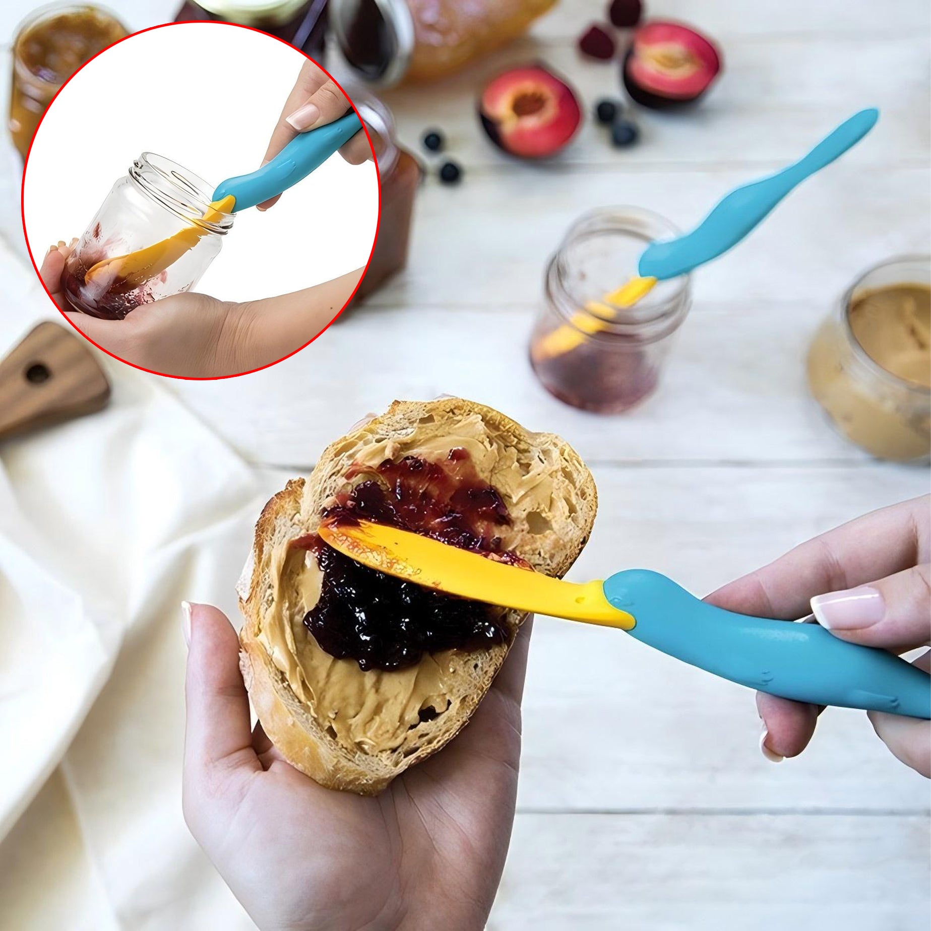 Hands using blue and yellow silicone spoons to spread peanut butter and jelly on a piece of bread, with jars of peanut butter and jelly in the background.