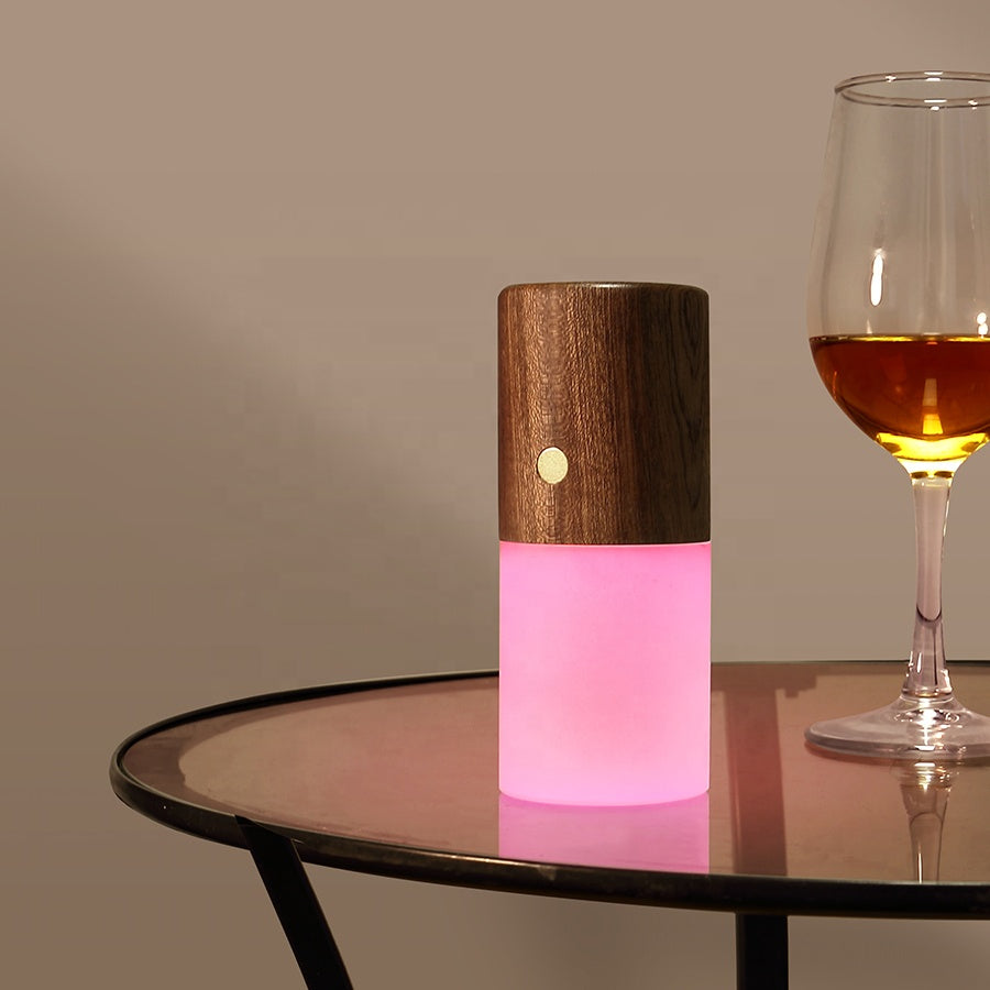 Wooden lamp with pink base on a table next to a glass of wine. rechargeable RGB wooden table lamp Pakistan, gravity flip night light USB‑C.