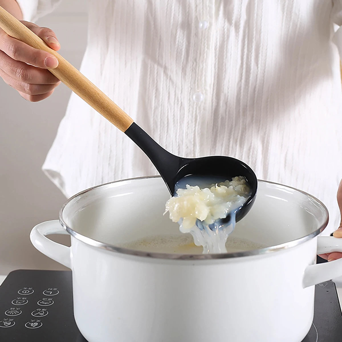 Person using a black ladle with a wooden handle to serve food from a pot on a stove. silicone wooden handle kitchen utensil set Pakistan.