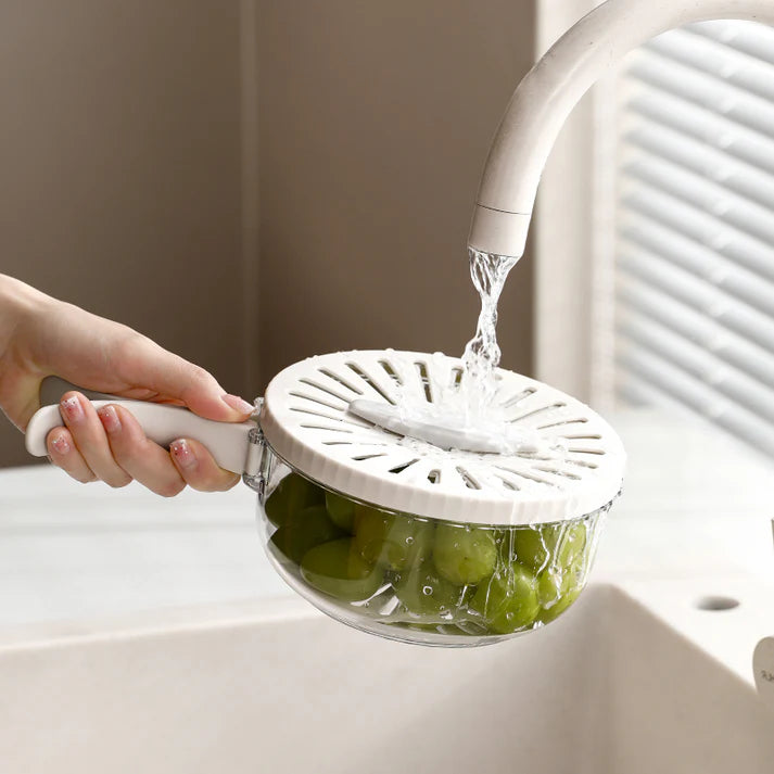 Person washing green grapes under running water using a white colander.