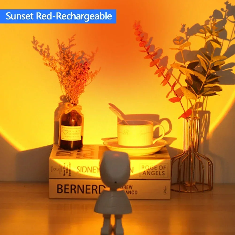 Decorative setup with books, a cup, and plants under a warm light, labeled 'Sunset Red-Rechargeable'. sunset lamp astronaut projector Pakistan, sunset projection lamp