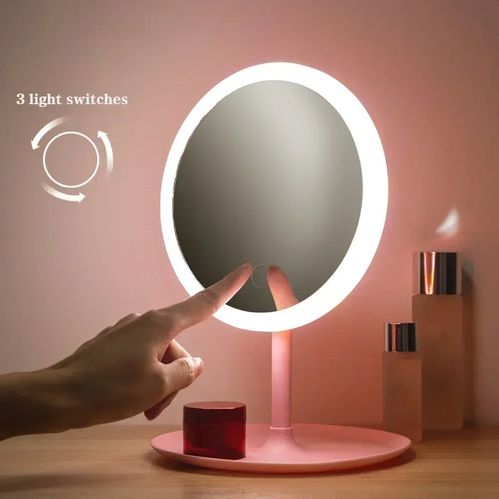 Person adjusting a round illuminated makeup mirror with three light switches on a pink background.