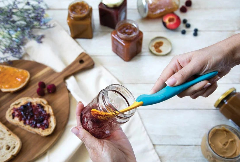 Person spreading jam on bread with a jar of jam and a platypus jar scraper, peanut butter scraper tool, waste free kitchen gadget, OTOTO jar spatula, jam spreader Pakistan